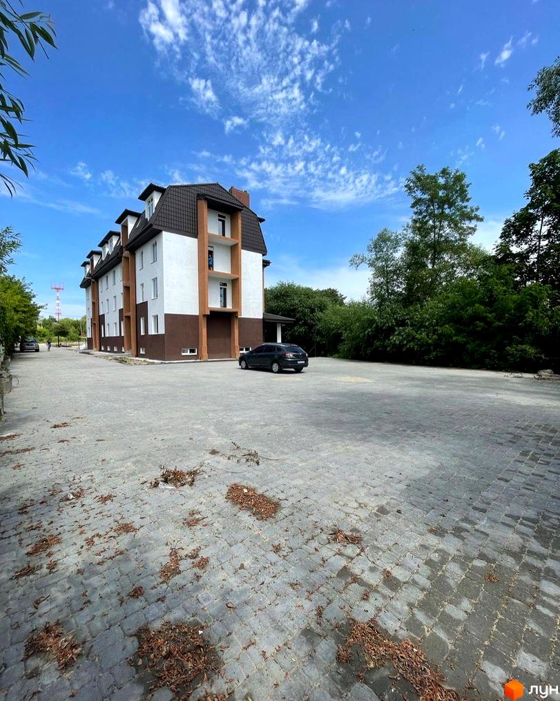 Зображення фасаду та прибудинкової території Новобудови Три шоколади. На передньому плані велика парковка з бруківки.