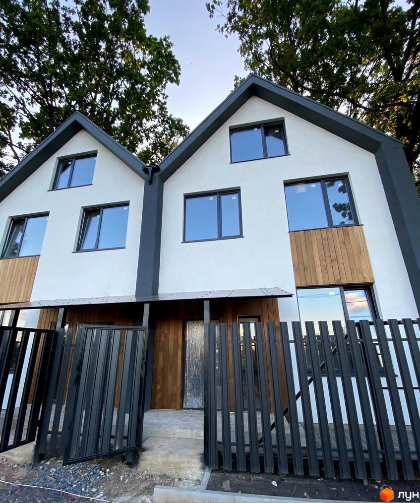 Зовнішній вигляд дуплексу в житловому комплексі. Білі стіни з дерев'яними вставками, темний дах та паркан.