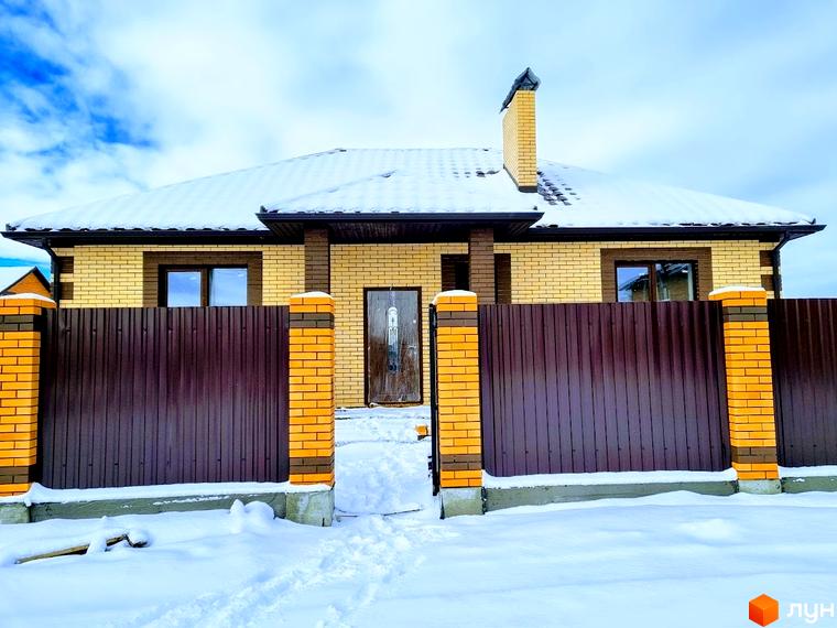 Котеджне містечко Green city: цегляний будинок з дахом, вкритим снігом. Перед будинком коричневий паркан та засніжена ділянка.