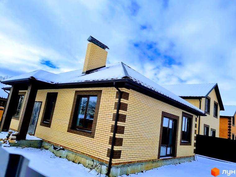Будинок Котеджного містечка Green city з фасадом з жовтої цегли, темними віконними рамами та дахом, вкритим снігом. Прибудинкова територія засніжена.