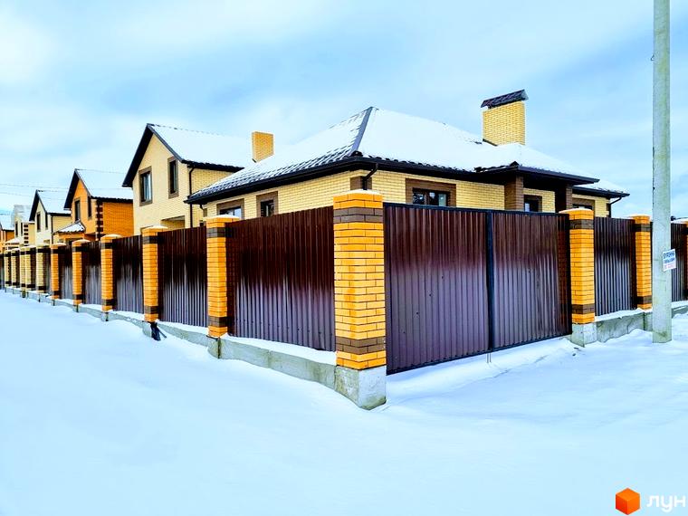 Будинки Котеджного містечка Green city зі світлої цегли та темними дахами під снігом. Перед ними коричневий паркан з цегляними стовпами на засніженій території.