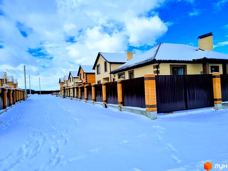 Ряд двоповерхових будинків з бежевої цегли та темними дахами в Котеджному містечку Green city. Засніжена вулиця з огорожами та стовпами.