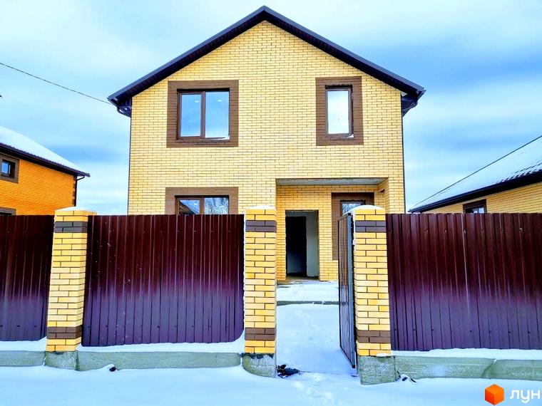 Котеджне містечко Green city: двоповерховий будинок з жовтої цегли та коричневим дахом. Територія огороджена коричневим парканом з цегляними стовпами, вкрита снігом.
