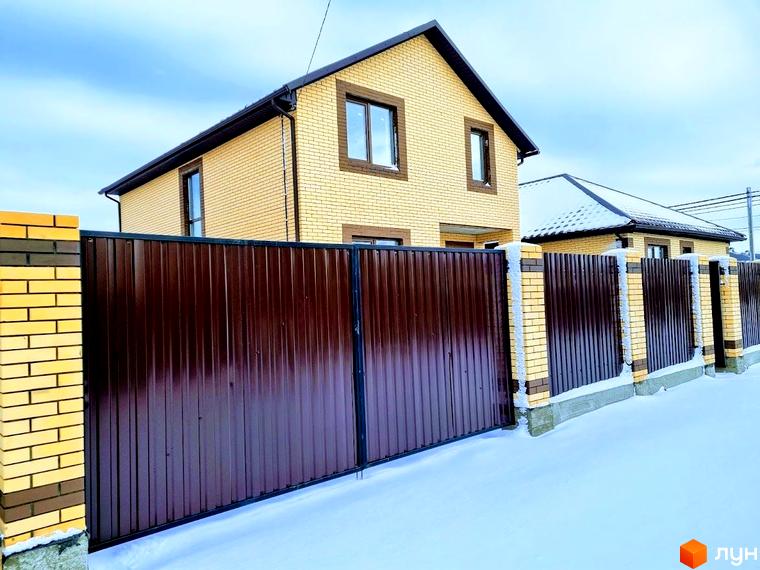 Двоповерховий будинок з жовтої цегли та коричневим дахом у Котеджному містечку Green city. Перед будинком коричневий металевий паркан та сніг.