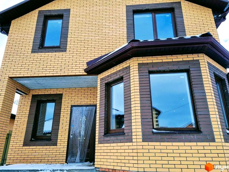 Двоповерховий будинок Котеджного містечка Green city з фасадом з жовтої цегли, коричневими вікнами та еркером. На прибудинковій території видно сніг.
