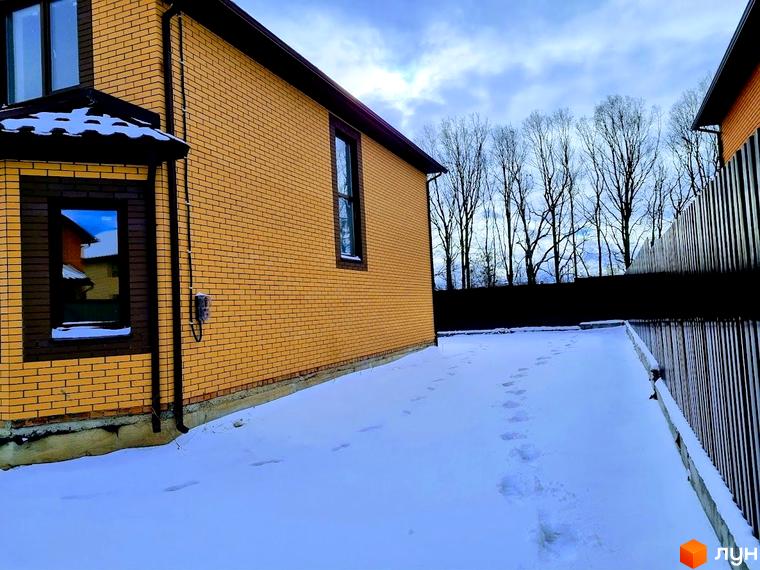 Котеджне містечко Green city: будинок з жовтої цегли та прибудинкова територія, вкрита снігом зі слідами.