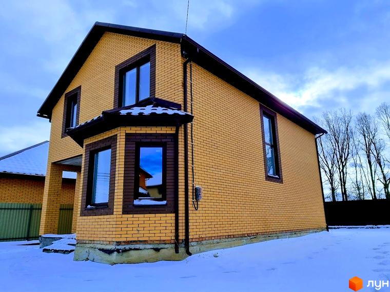 Двоповерховий будинок з жовтої цегли з коричневими вікнами та дахом на засніженій ділянці Котеджного містечка Green city.