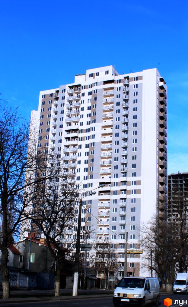 Високоповерховий житловий комплекс Альтаїр 2 з сірими та білими фасадами, численними балконами та великими вікнами. Навколо будівлі видно дерева та міську забудову.