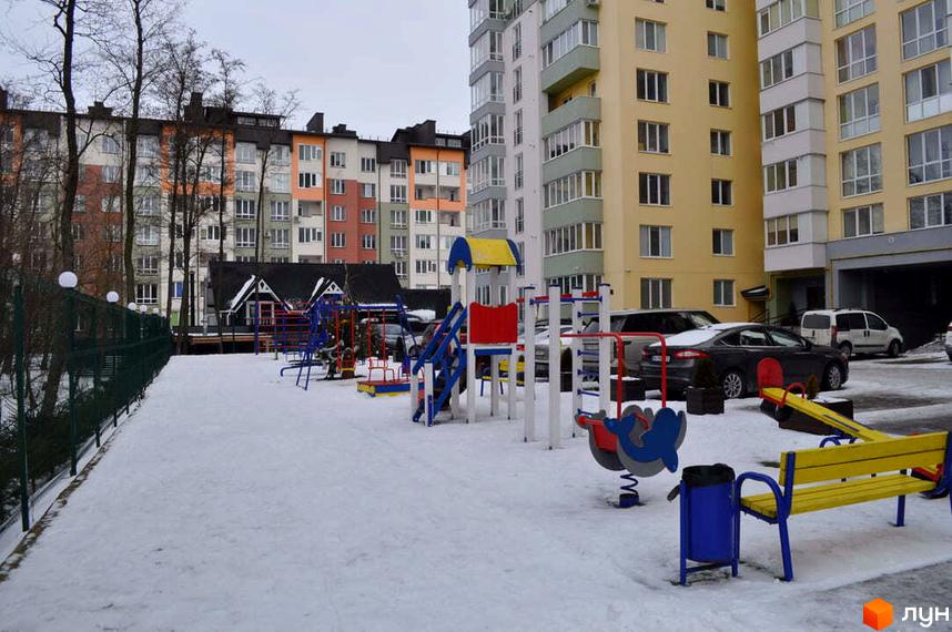 Житловий комплекс Монако: різнокольорові багатоповерхові будинки з численними вікнами. Прибудинкова територія вкрита снігом, є дитячий майданчик та автомобілі.