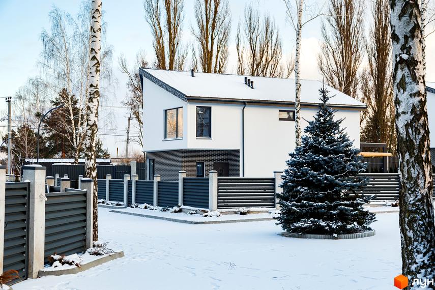 Котеджне містечко КМ Friends Club взимку. Білий двоповерховий будинок з сірим цегляним цоколем, огороджена територія з ялинкою.