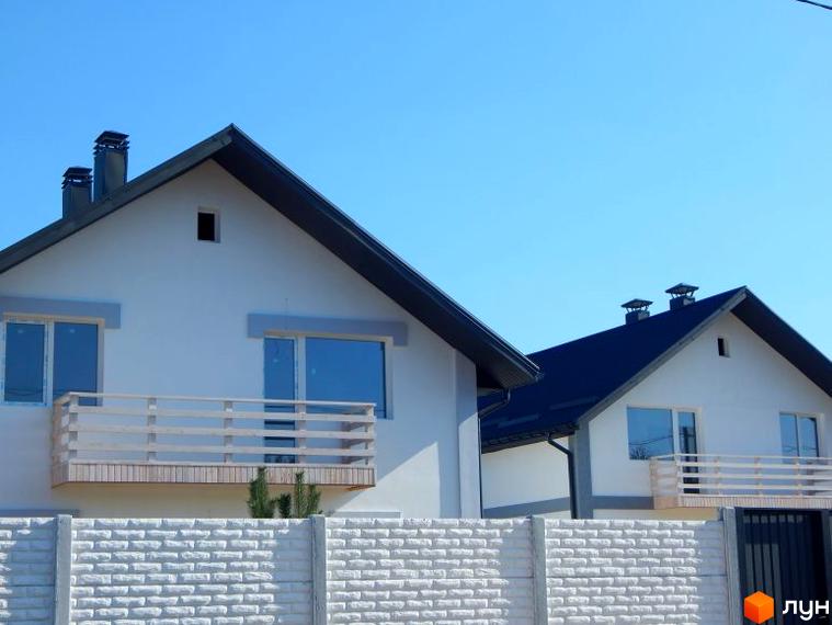 Двоповерховий будинок з балконом та білою цегляною огорожею. На задньому плані видно КМ Черкаські Тишки, що потопає у зелені та сонячному світлі.