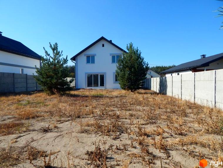 Білий двоповерховий будинок з темним дахом у Містечку котеджів Черкаські Тишки. Поряд з будинком суха трава та бетонний паркан.