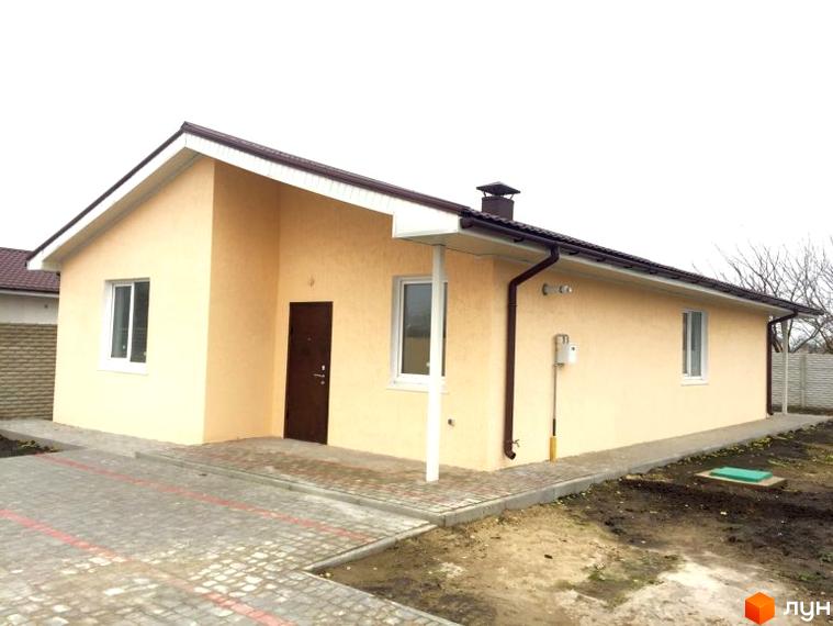 Одноповерховий будинок з бежевими стінами та коричневим дахом. Перед будинком викладена бруківка, поруч газон та огорожа.