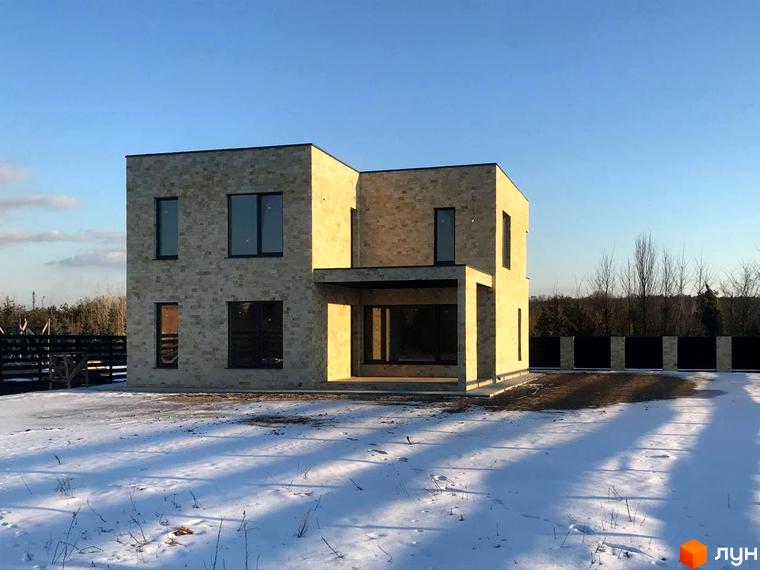 Двоповерховий будинок з великими вікнами, облицьований світлим каменем. Навколо будинку сніг та чорний паркан.