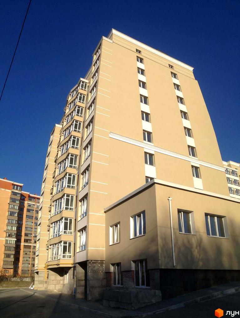 Зовнішній вигляд багатоповерхової новобудови на вул. Зарічанська, 3/3б, з фасадом світло-бежевого кольору та численними вікнами. Поруч видно іншу цегляну будівлю.