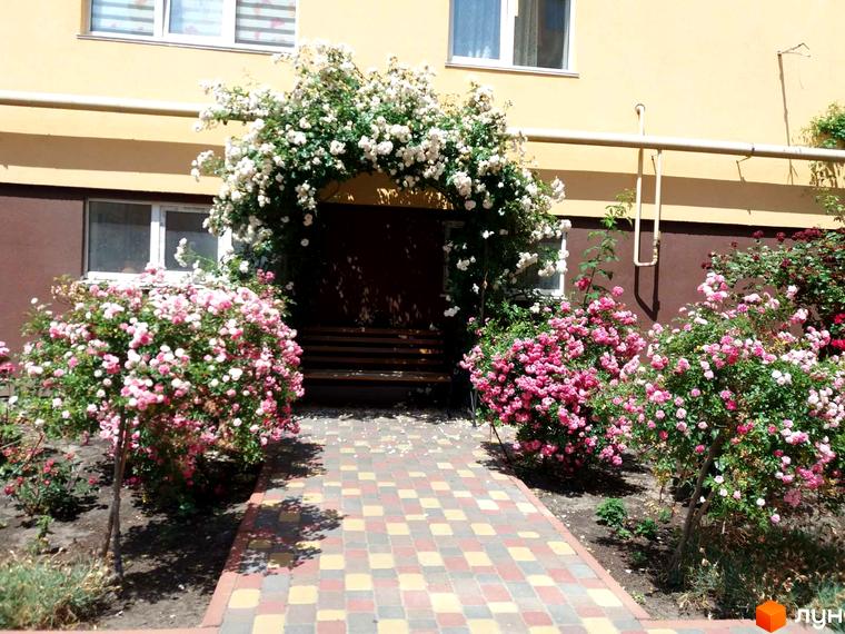 Житловий комплекс Київський маєток з аркою з білих квітів та кущами рожевих троянд. Вхід до будинку прикрашений квітковою аркою та доріжкою з плитки.