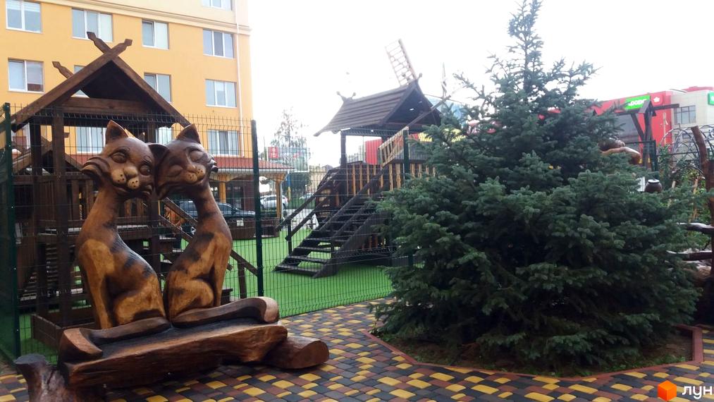 Житловий комплекс Київський маєток: дитячий майданчик з дерев'яними скульптурами котів та ялинкою. Будинок на тлі.