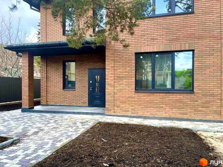 Котеджне містечко Дубовий Гай: фасади будинків з червоної цегли, вікна з темними рамами та вимощена бруківкою прибудинкова територія. Будівельний проєкт з зеленими насадженнями.