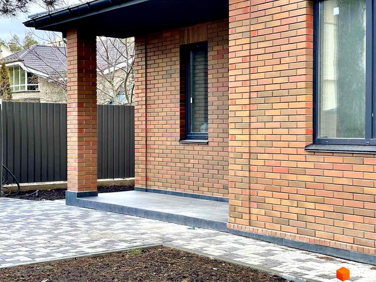 Котеджне містечко Дубовий Гай: фасад будинку з цегляним оздобленням та прибудинкова територія з бруківкою.