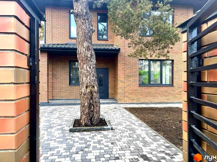 Котеджне містечко Дубовий Гай: двоповерховий будинок з цегляним фасадом та прибудинковою територією з бруківки та зеленої зони.