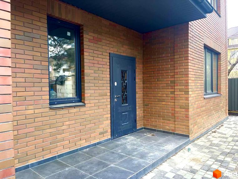 Фасад будинку котеджного містечка КМ Дубовий Гай з цегляним оздобленням, темними вікнами та дверима. Поруч розташована вимощена плиткою прибудинкова територія.