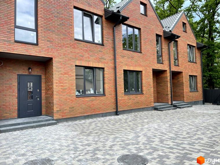 Зовнішній вигляд таунхаусів Новий Brighton з червоної цегли та сірого бруківки на прибудинковій території. Комплекс має сучасні вікна та двері.