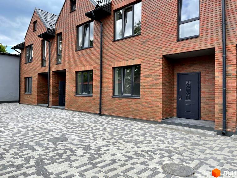 Таунхауси Новий Brighton з червоної цегли та сірим мощенням перед будинками. Зовнішній вигляд новобудови та прибудинкової території.