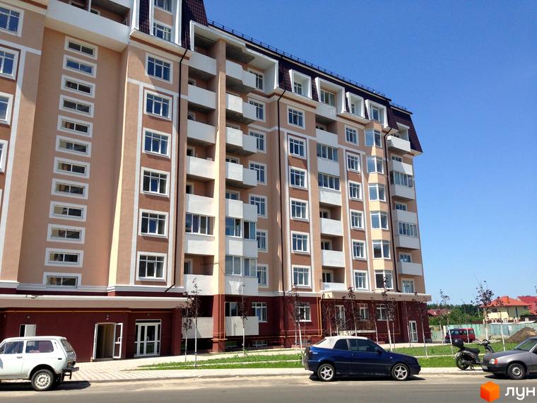 Житловий комплекс Варшавський двір має бежевий фасад з білими вікнами та балконами. Перед будинком розташовані дорога, тротуар та молоді дерева.