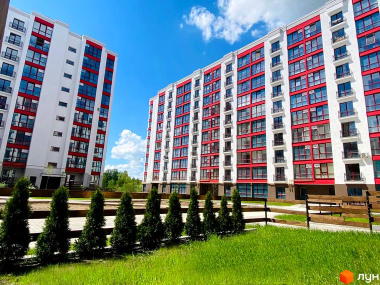 Житловий комплекс Містечко Козацьке з білими фасадами та червоними акцентами. На прибудинковій території зелені насадження та доглянутий газон.