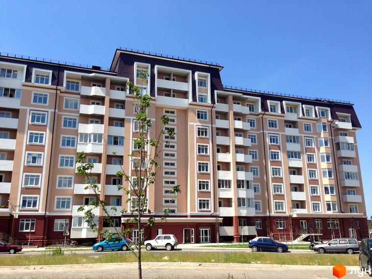 Житловий комплекс Варшавський двір з фасадом, що має великі вікна. Прибудинкова територія з автомобілями та зеленими насадженнями.