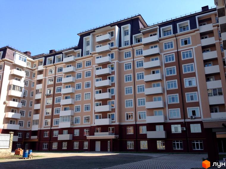 Житловий комплекс Варшавський двір - багатоповерховий будинок з балконами та вікнами на тлі блакитного неба. На прибудинковій території видно паркування та огорожу.