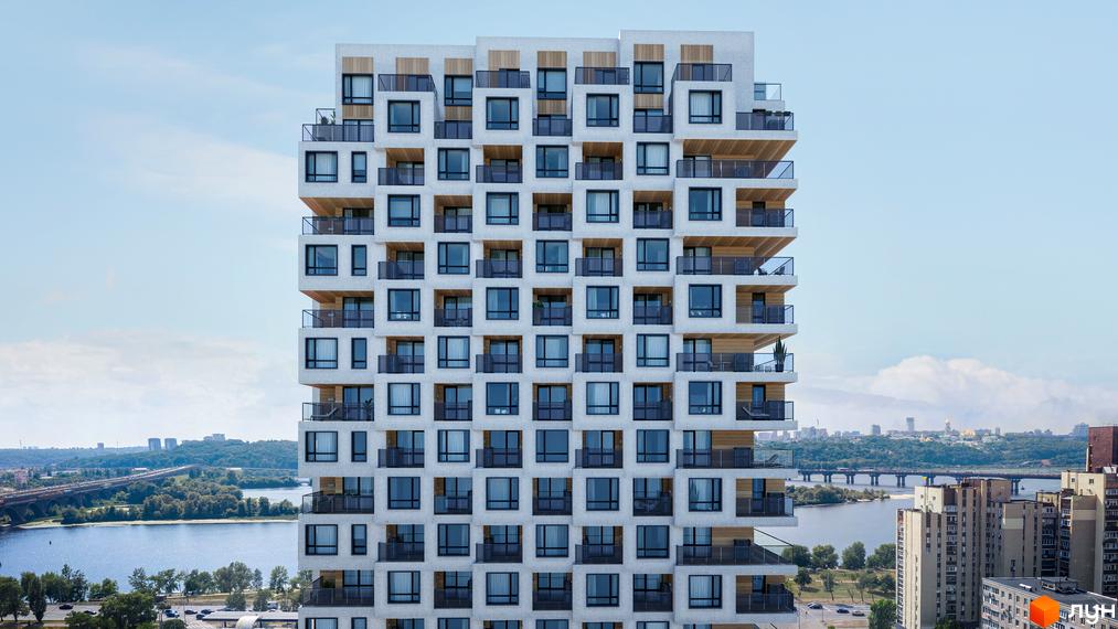 Висотна будівля житлового комплексу Kub29 з великою кількістю вікон та балконів з видом на річку та місто.