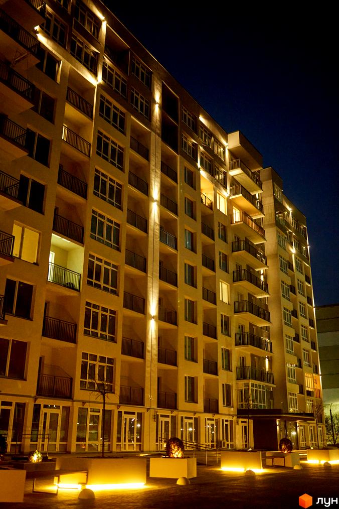 Зображення фасаду багатоповерхового будинку вночі. Житловий комплекс KromaxBud з балконами та освітленням прибудинкової території.