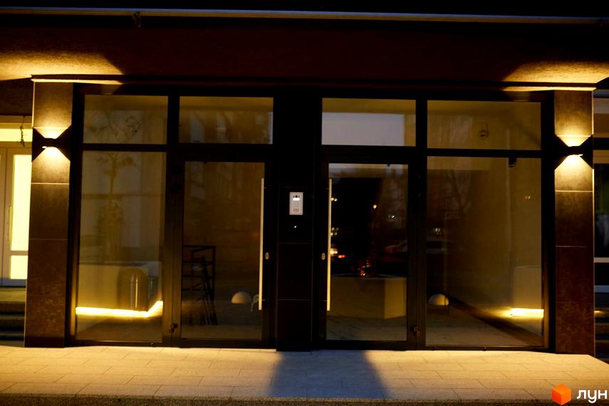 Новобудова ЖК KromaxBud з двома вхідними дверима та освітленням фасаду. Прибудинкова територія освітлена лінійною підсвіткою.