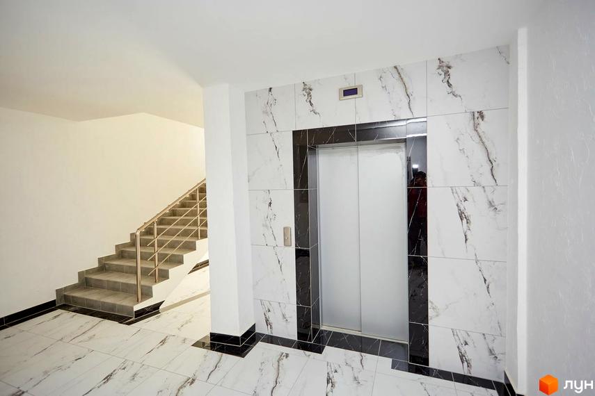 Інтер'єр холу Новобудови KromaxBud з ліфтом та сходами. Оздоблення стін та підлоги виконано з плитки під мармур.