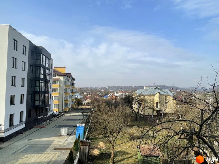 Новобудова ЖК Center з фасадами білого та сірого кольорів, вікнами з панорамним склінням, розташована на фоні міського пейзажу. Прибудинкова територія з бруківкою та зеленими насадженнями.