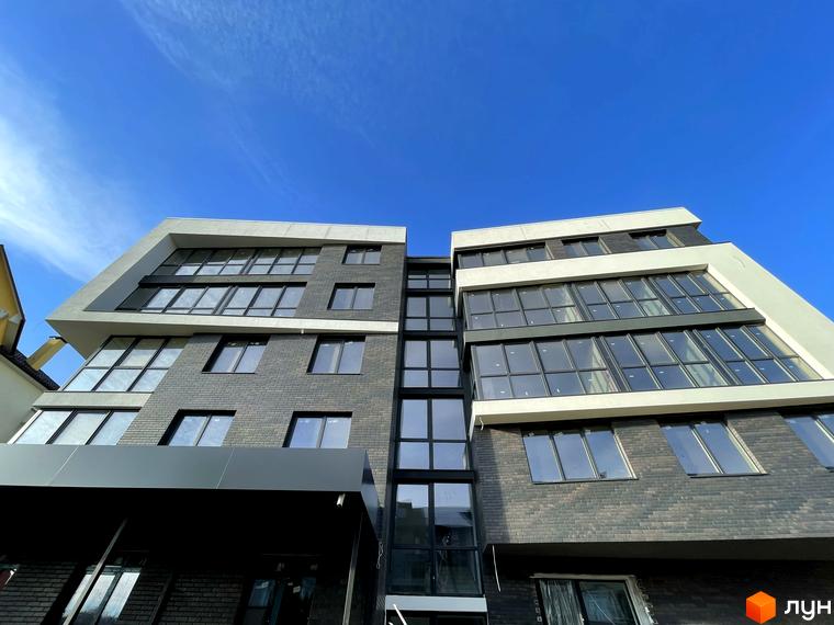 Фасад житлового комплексу Center з панорамними вікнами та цегляним оздобленням під блакитним небом. Сучасна архітектура новобудови.