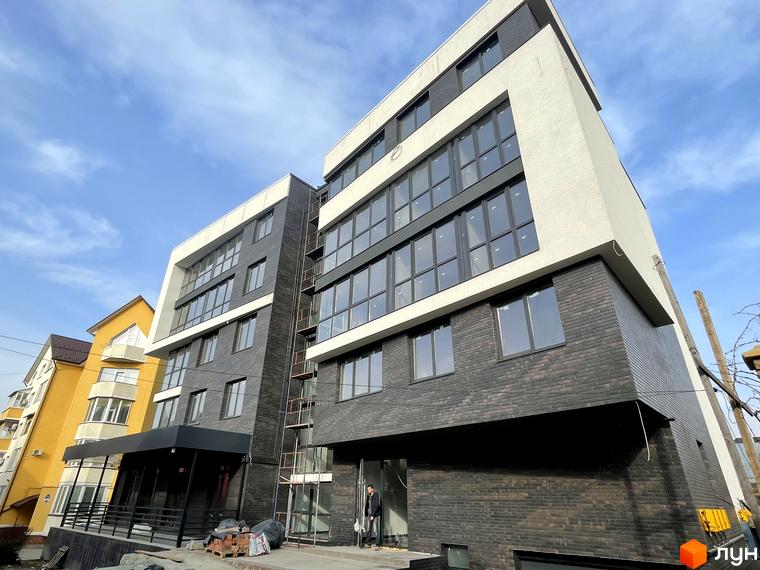 Зовнішній вигляд житлового комплексу Center з цегляним фасадом та великими вікнами. Поруч розташована жовта будівля та вхідна група.