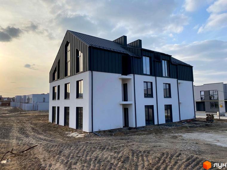 Зовнішній вигляд новобудови ЖК Струмочок 2 з білими стінами та темним дахом. Навколо будівельний майданчик з піщаною землею.