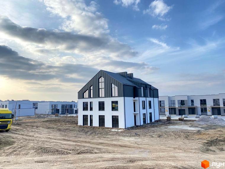 Будівельний проєкт ЖК Струмочок 2. Сучасні будинки з сірим дахом та білими фасадами на тлі хмарного неба. Територія забудови з будівельною технікою та будматеріалами.