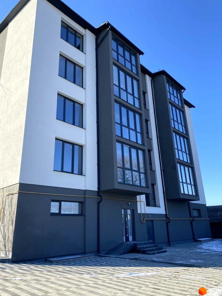 Зовнішній вигляд багатоповерхового будинку. Фасад будівлі пофарбовано у білий та сірий кольори. Перед будинком розташована бруківка.