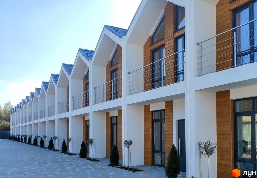 Ряд двоповерхових будинків з білими фасадами, дерев'яними вставками та балконами. Перед будинками викладена бруківка, ростуть невеликі дерева.