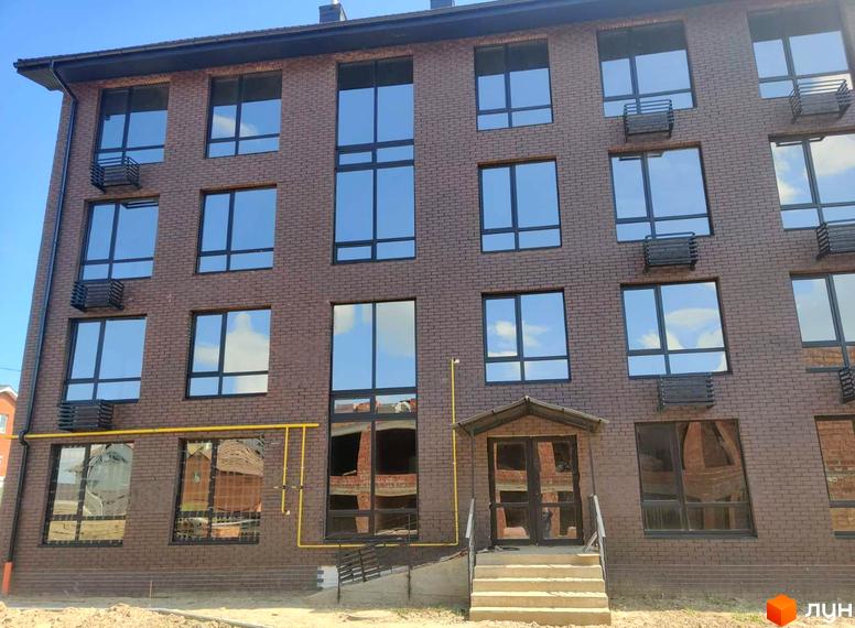 Зовнішній вигляд багатоквартирного будинку в Житловому районі Моя Баварія. Фасад будинку оздоблений коричневою цеглою, великі вікна з чорними рамами.