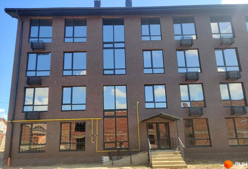 Фасад новобудови ЖК Моя Баварія з коричневої цегли, великими вікнами та кондиціонерами. Поруч розташована прибудинкова територія з входом та сходами.