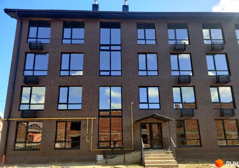 Фасад житлового комплексу Моя Баварія з цегляною обробкою та великими вікнами. Перед будинком розташовані сходи та навіс над входом.