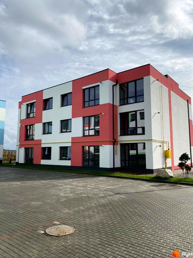 Зовнішній вигляд новобудови ЖК Стайл Хаус з червоно-білим фасадом та великими вікнами. Прибудинкова територія з бруківкою та зеленими насадженнями.