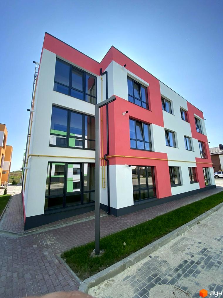 Новобудова ЖК Стайл Хаус з біло-рожевим фасадом та великими вікнами, розташована на тлі блакитного неба. Поруч бруківка та зелена галявина.