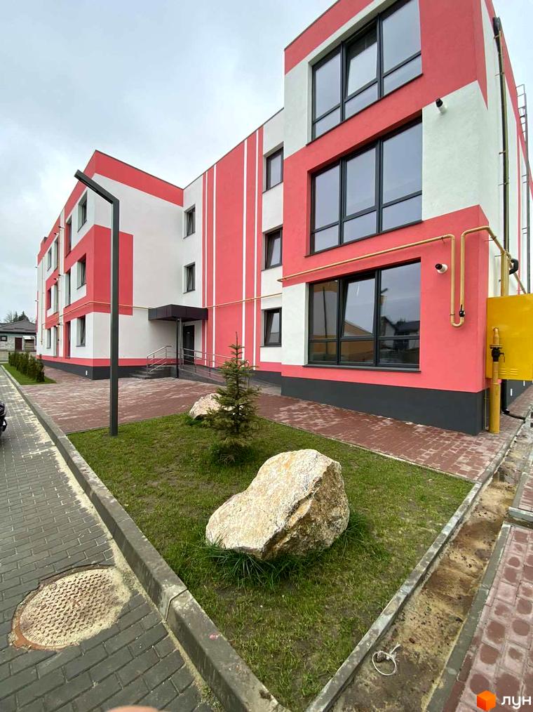 Житловий комплекс Стайл Хаус: фасади будинку в біло-рожевих тонах з великими вікнами, прибудинкова територія з газоном та великим каменем.