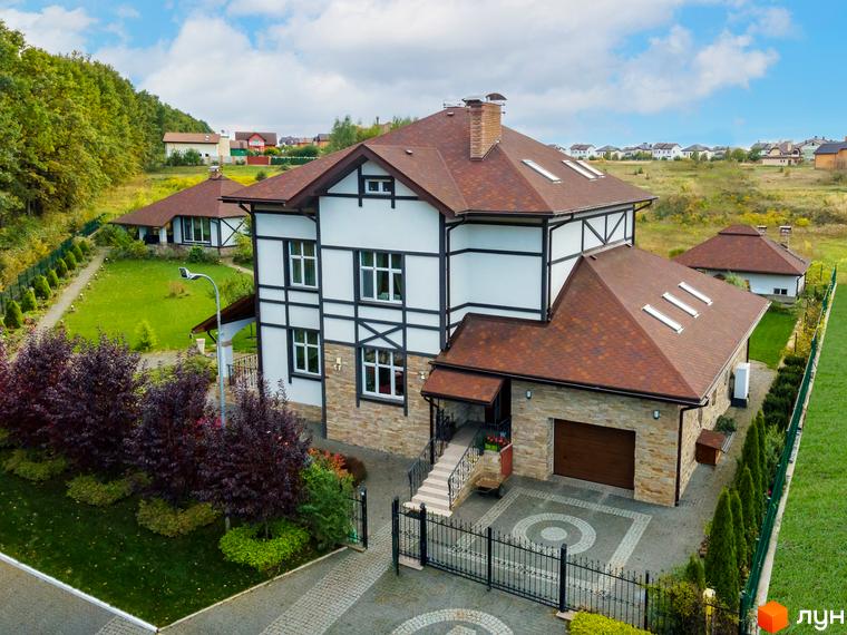 Котеджне містечко КМ Home Resort: двоповерховий будинок з коричневим дахом, білими стінами та кам'яним цоколем, огороджена територія з доглянутим газоном та деревами.