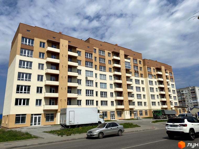 Зовнішній вигляд новобудови на вул. Володимира Великого, 5б, з балконами та великою кількістю вікон. На прибудинковій території видно автомобілі та вантажівку.